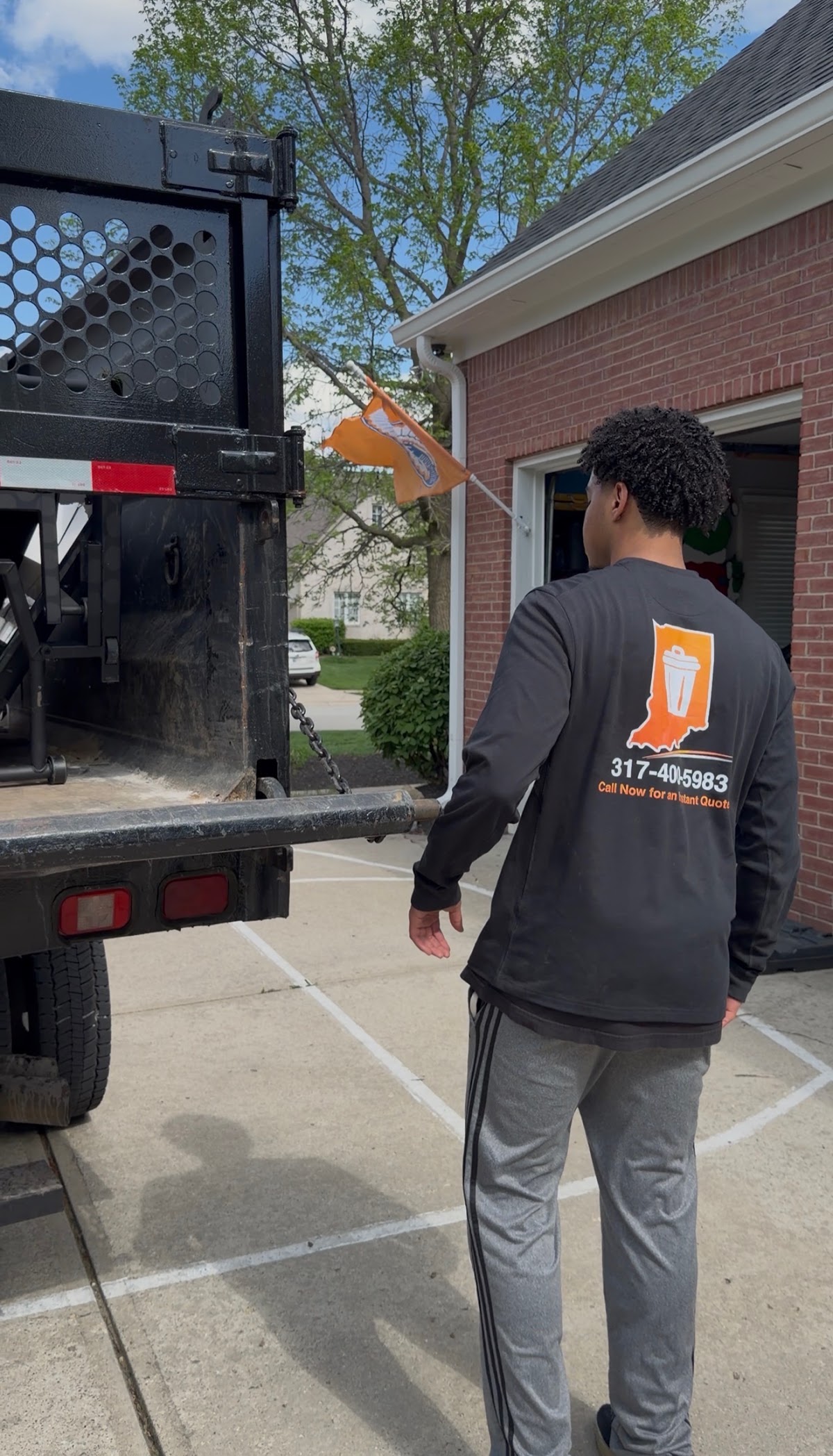 A crew member in a branded Hoosier Junk Pros shirt standing at the tailgate of the company&rsquo;s black flatbed dump truck.