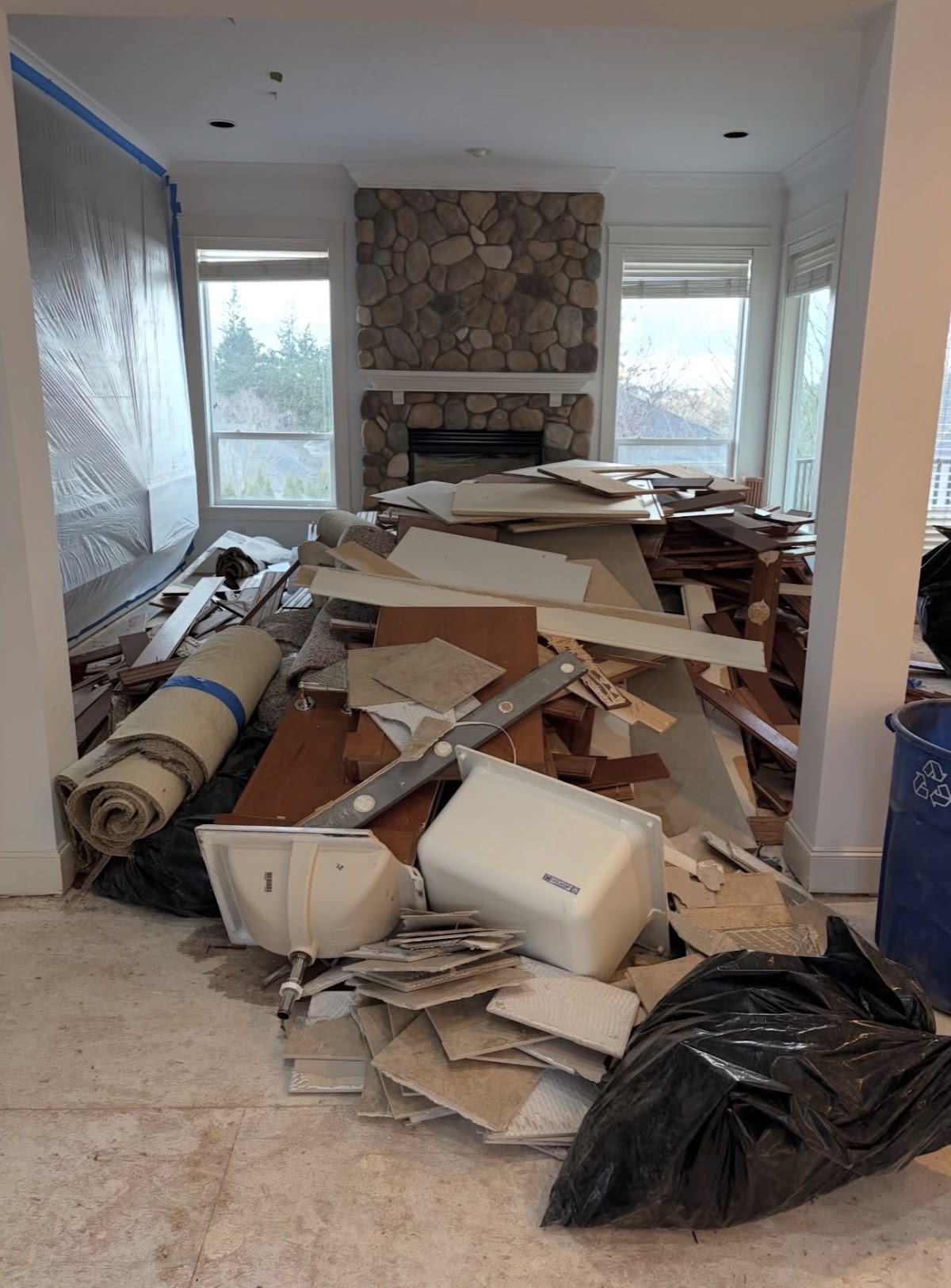 A living room full of remodel debris — torn-out cabinetry, a rolled carpet, tile and a removed toilet.